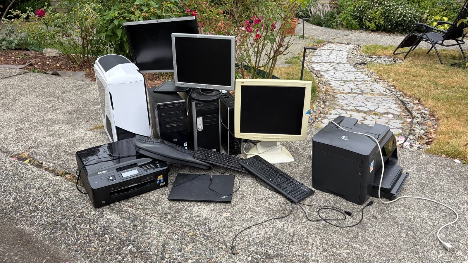 Monitors, towers, keyboards, and printers on a driveway