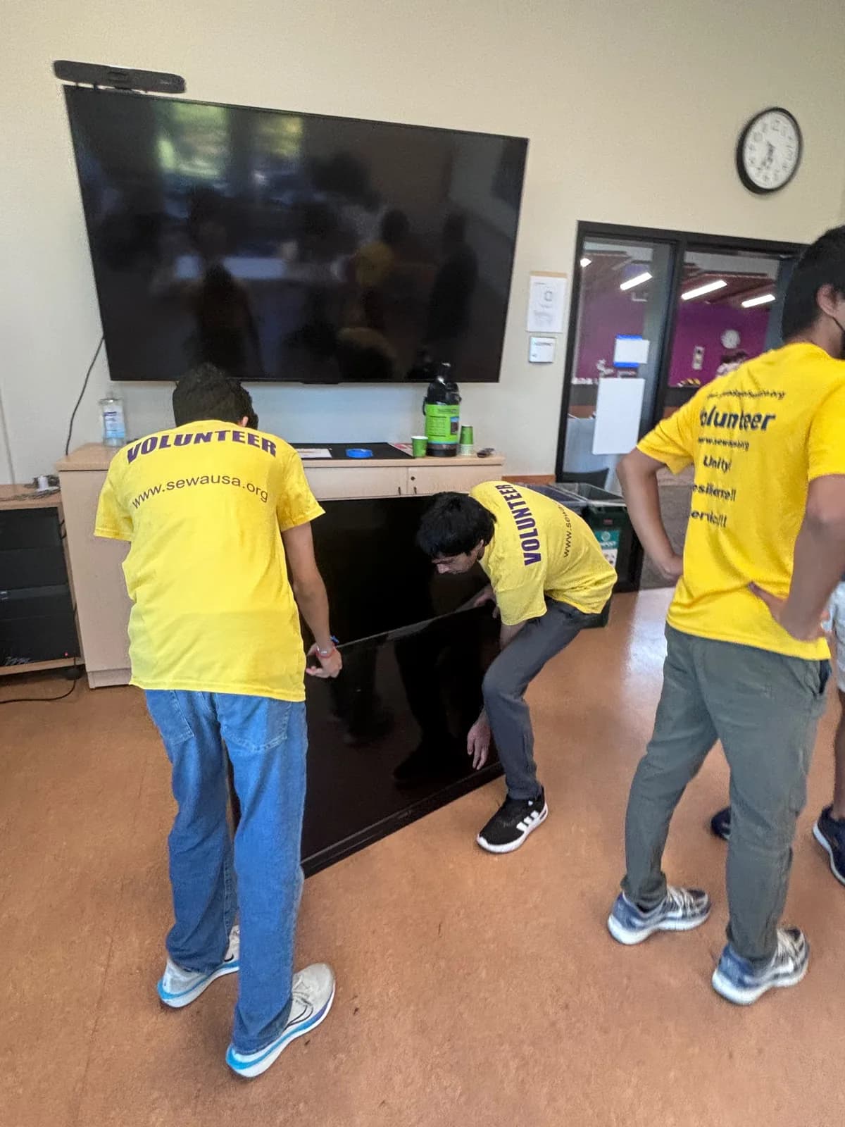 Volunteers in yellow shirts working together to lift a large flat-screen display